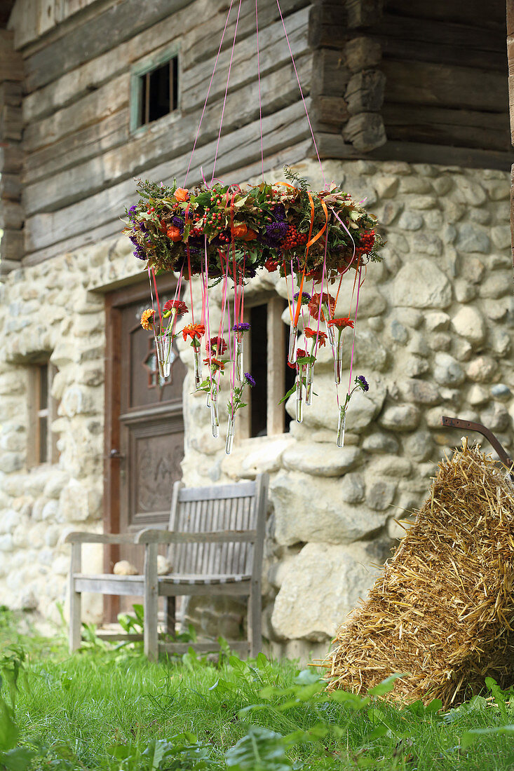 Autumnal wreath of flowers with test tubes hung from ribbons outside farmhouse