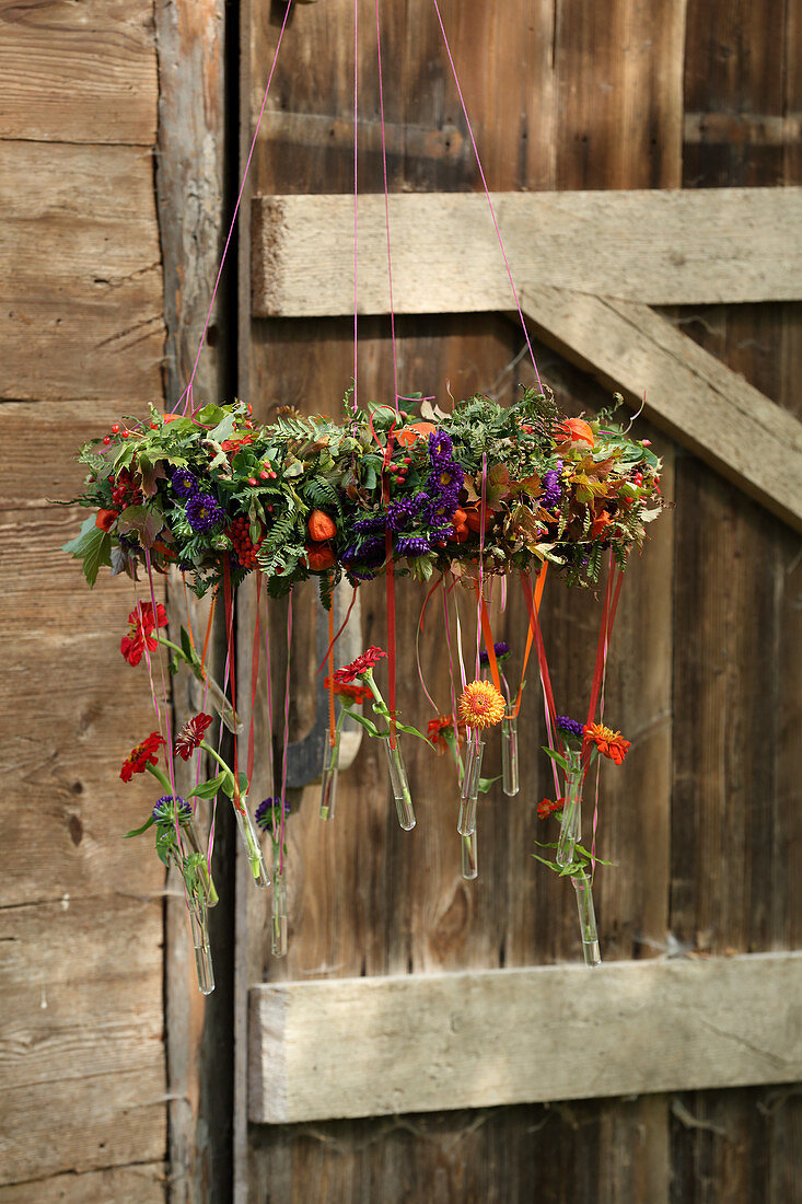 Autumnal wreath of flowers with test tubes hung from ribbons in front o ´f wooden door