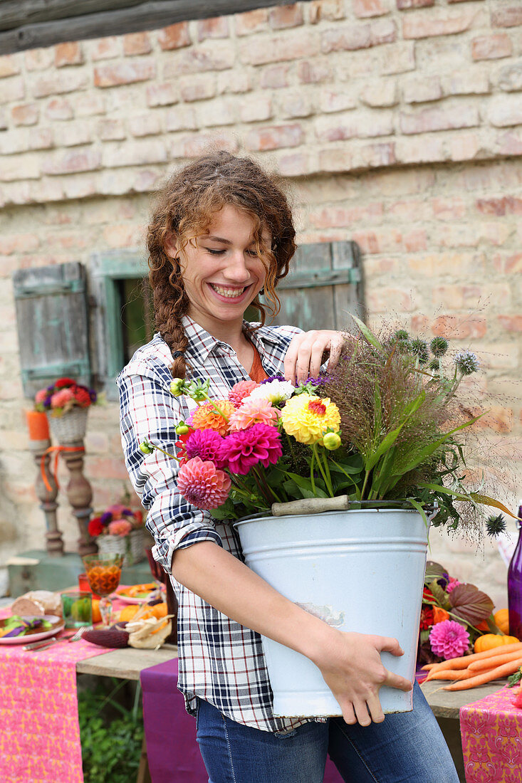 Lachende Frau trägt einen Eimer mit bunten Herbstblumen