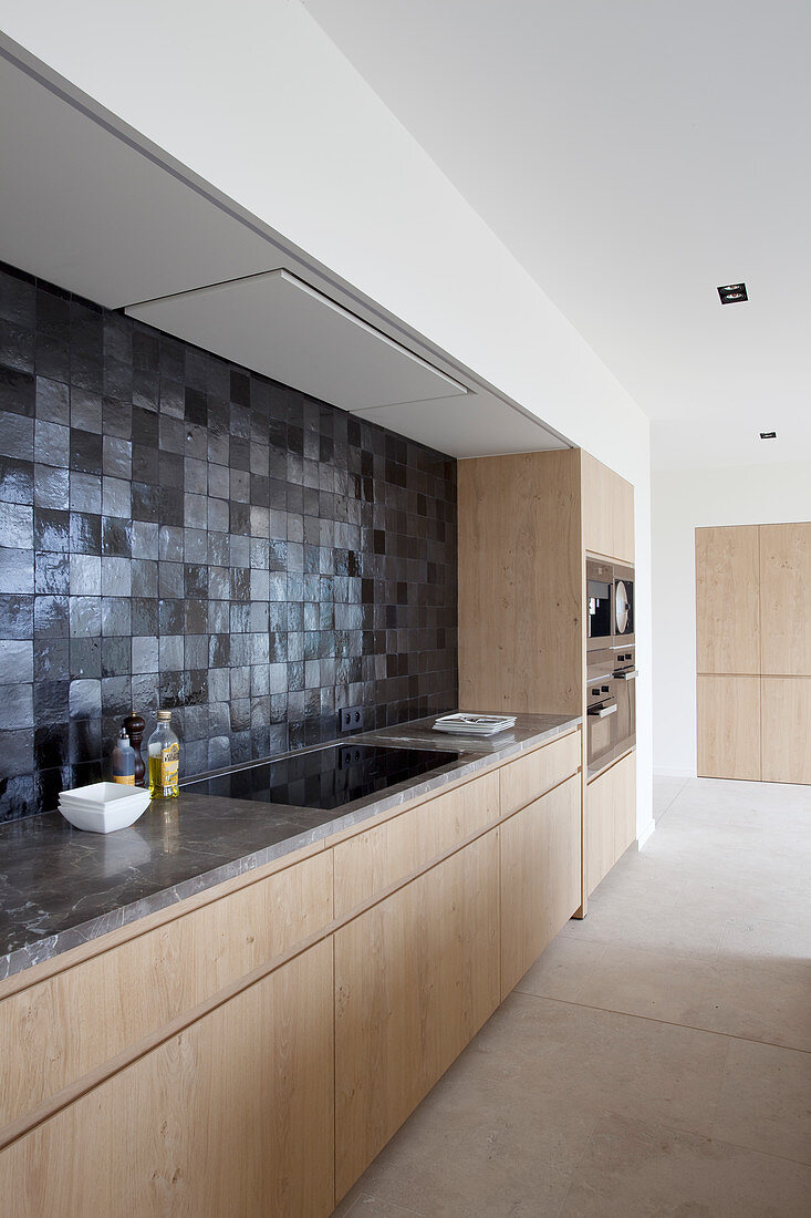 Modern fitted kitchen with wooden cabinets and black wall tiles