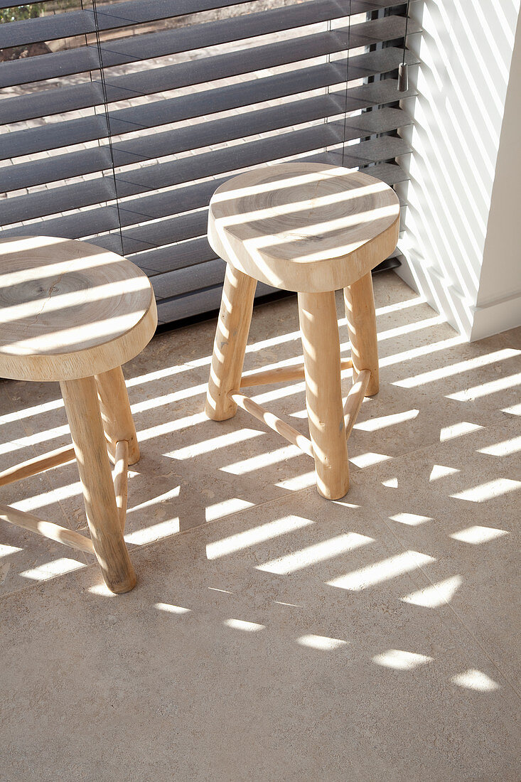 Two stools with tree-trunk seats next to window with louvre blinds