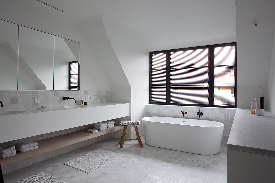 Free-standing bathtub below window and double washstand in spacious bathroom