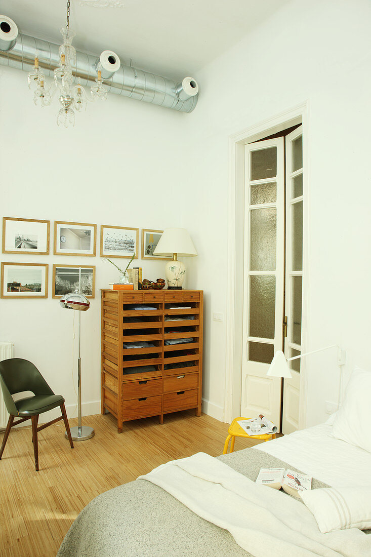Cabinet with open-fronted compartments below gallery of pictures in bedroom