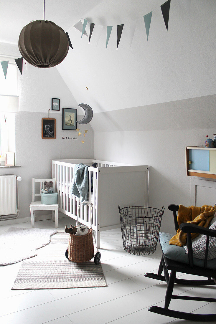 Weißes Gitterbett und Schaukelstuhl im Babyzimmer mit weißem Holzdielenboden
