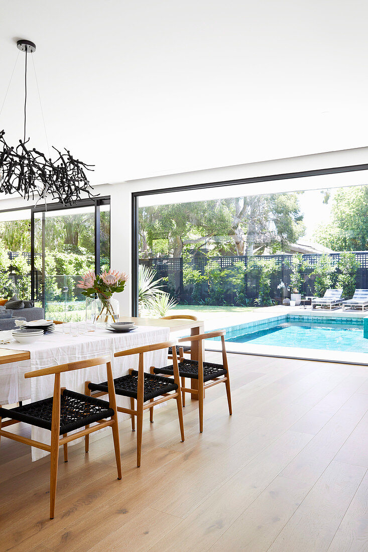 Dining table with designer chairs in front of the window facing the garden with pool