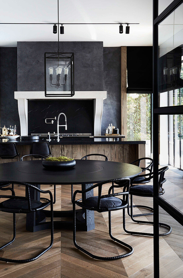 Runder, schwarzer Tisch mit passenden Stühlen in offener Küche