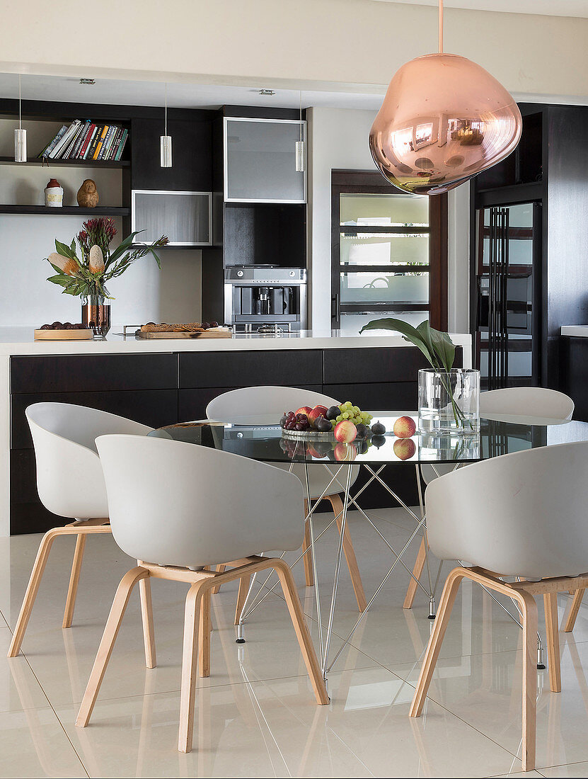 Essbereich mit rundem Glastisch und Designerstühlen vor Kücheninsel