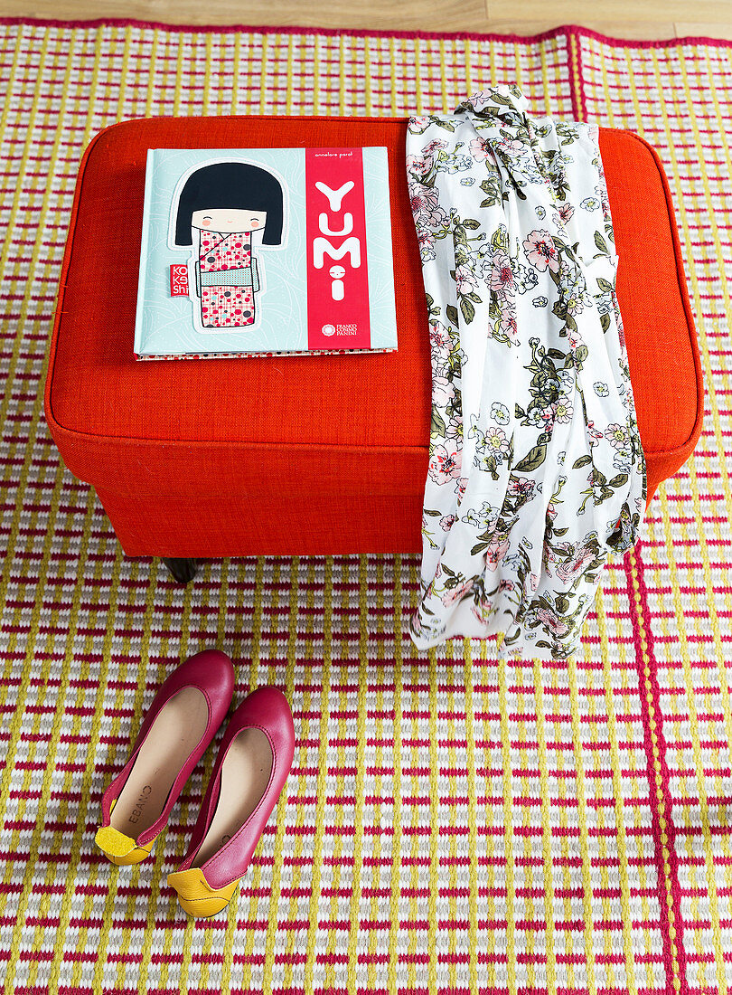 Book and dress on red pouffe and ballet flats on patterned rug