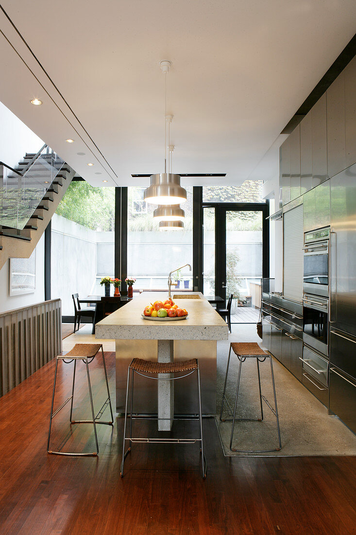 Stainless steel cabinets and island counter in fitted kitchen with dining area in front of terrace doors in background