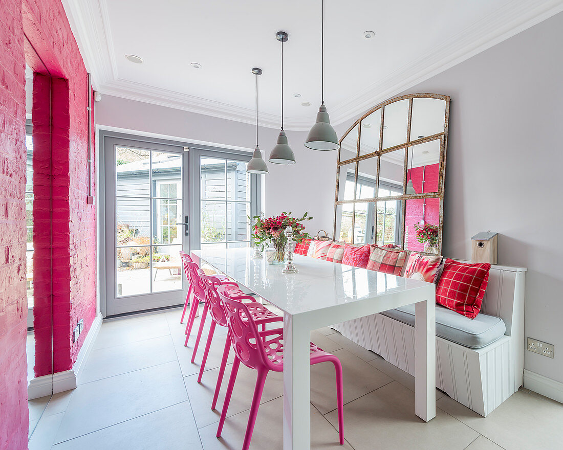 Hot-pink chairs and wall in bright dining room with large mirror