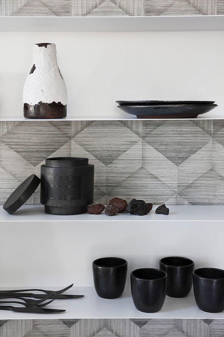 Crockery and cutlery on wall-mounted shelves on monochrome patterned wallpaper