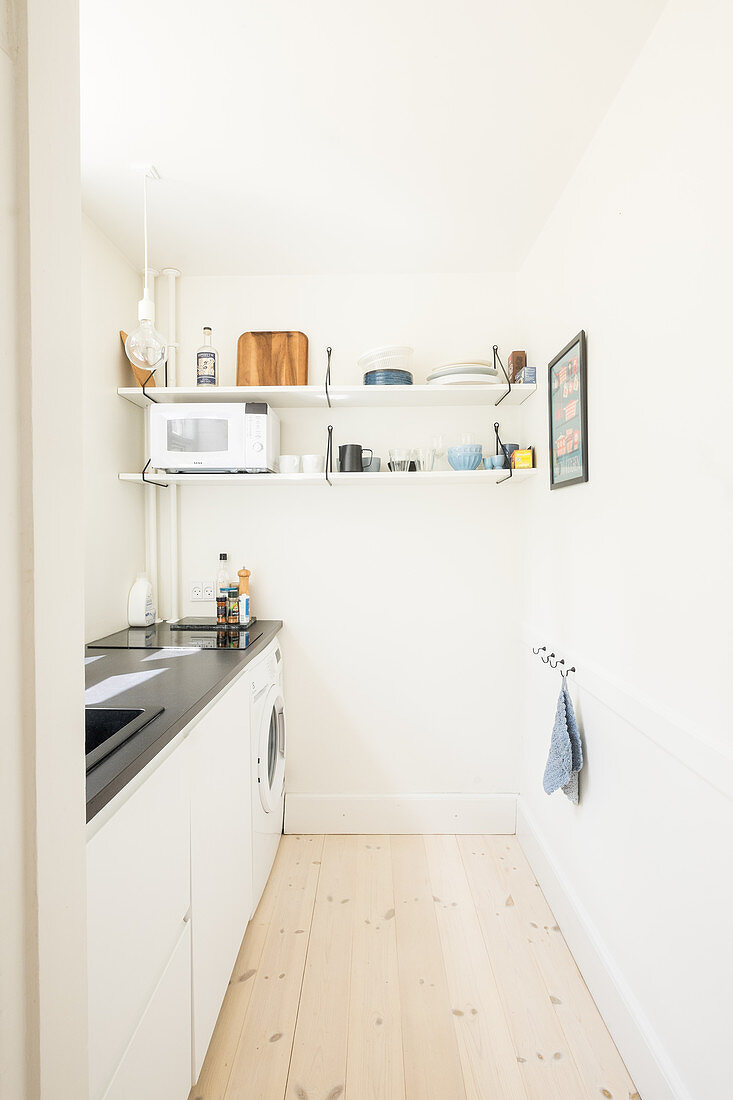 Small, narrow, white kitchen with black worksurface