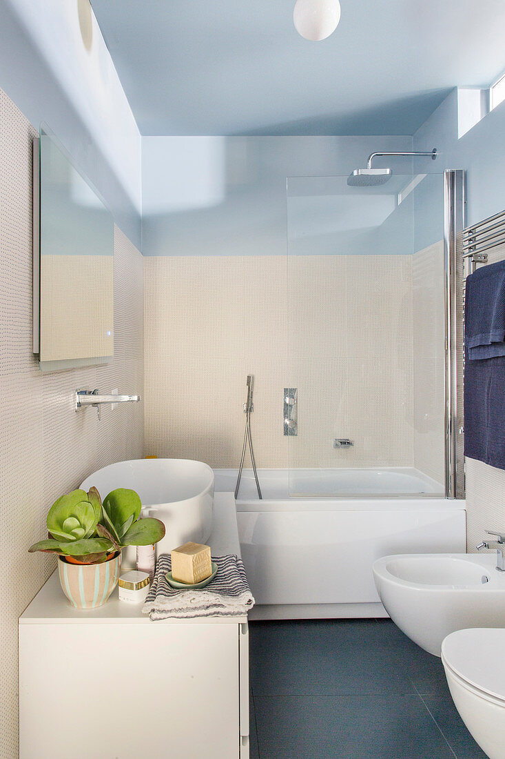 Washstand with countertop sink and bathtub in bathroom with pale wall tiles and sky-blue ceiling