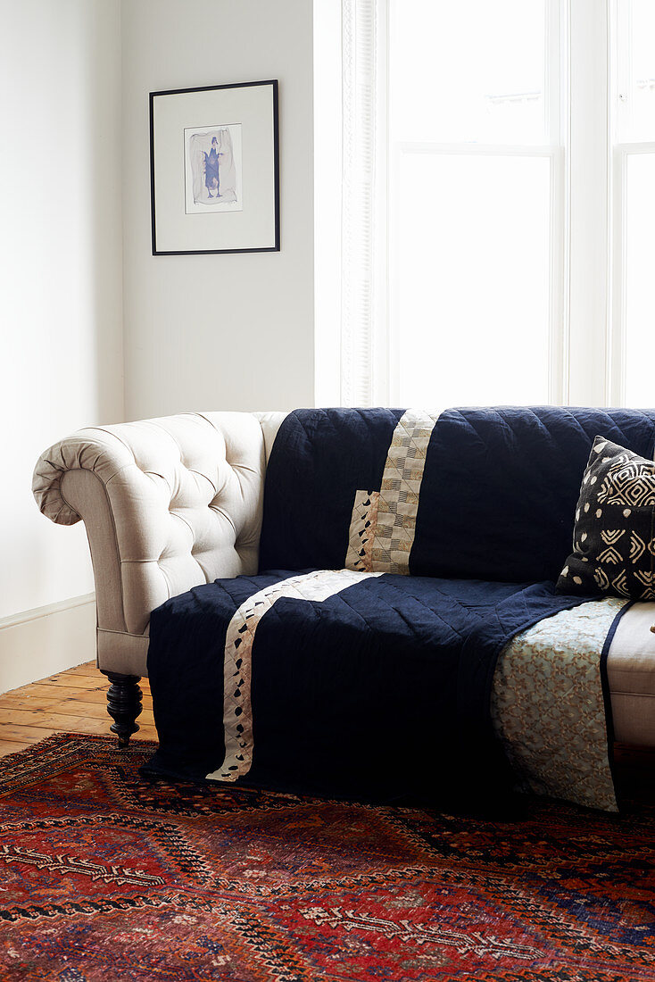 Helles, kaptioniertes Sofa mit dunkelblauem Quilt