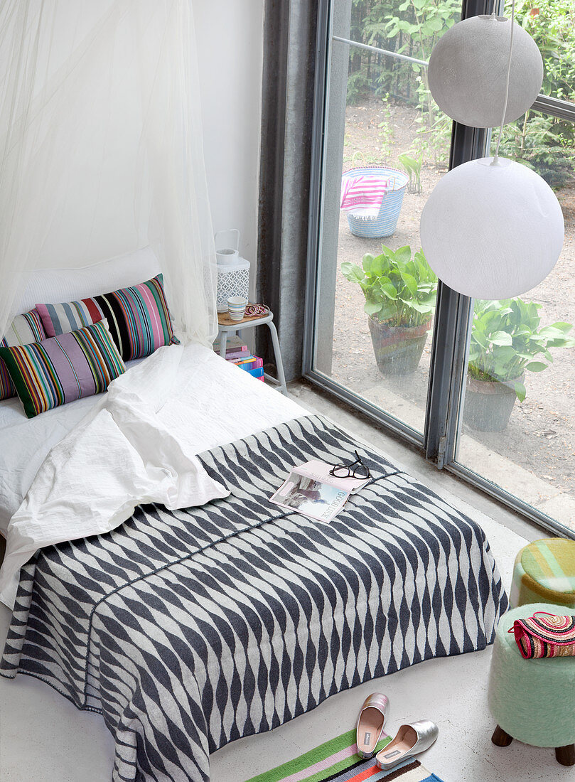 Blick auf Doppelbett mit schwarz-weiß gemusterter Tagesdecke und gestreiften Kissen vor Terrassentür