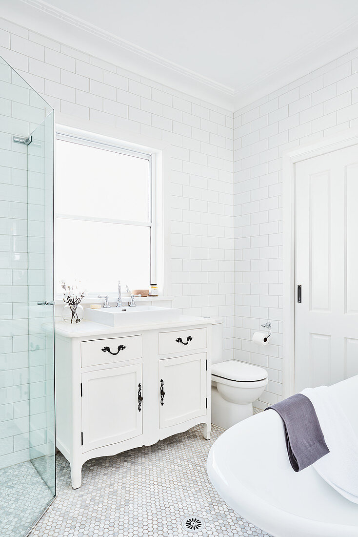 Washstand with countertop sink below window, toilet and free-standing bathtub in white bathroom