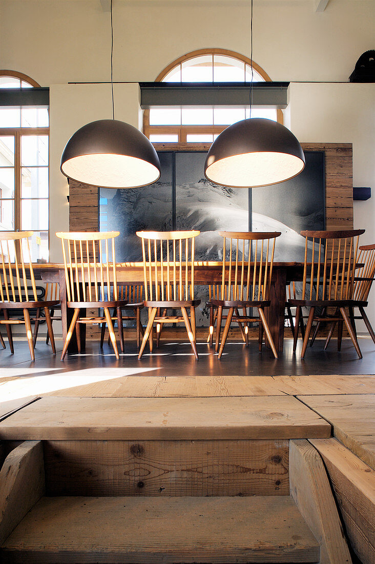 Long dining table and chairs below pendant lamps in converted loft