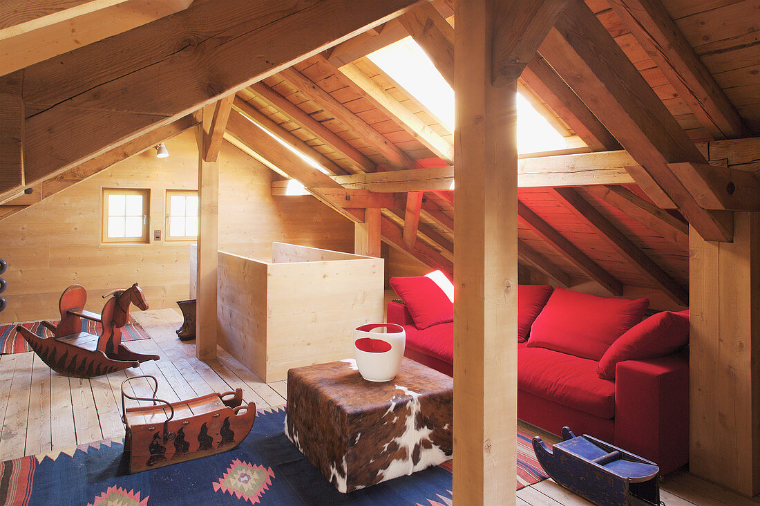 Rotes Sofa, Hocker mit Tierfell und Schaukelpferd im Dachzimmer mit Holzverkleidung