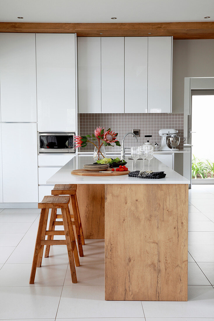 Elegante weiße Küche mit Kücheninsel und Barhockern aus Holz