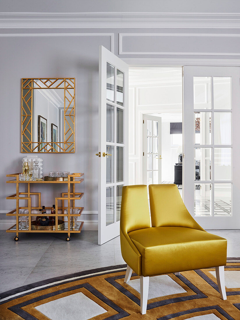 Goldfarbener Designerstuhl auf Teppich, im Hintergrund Spiegel und Barwagen in passenden Farben