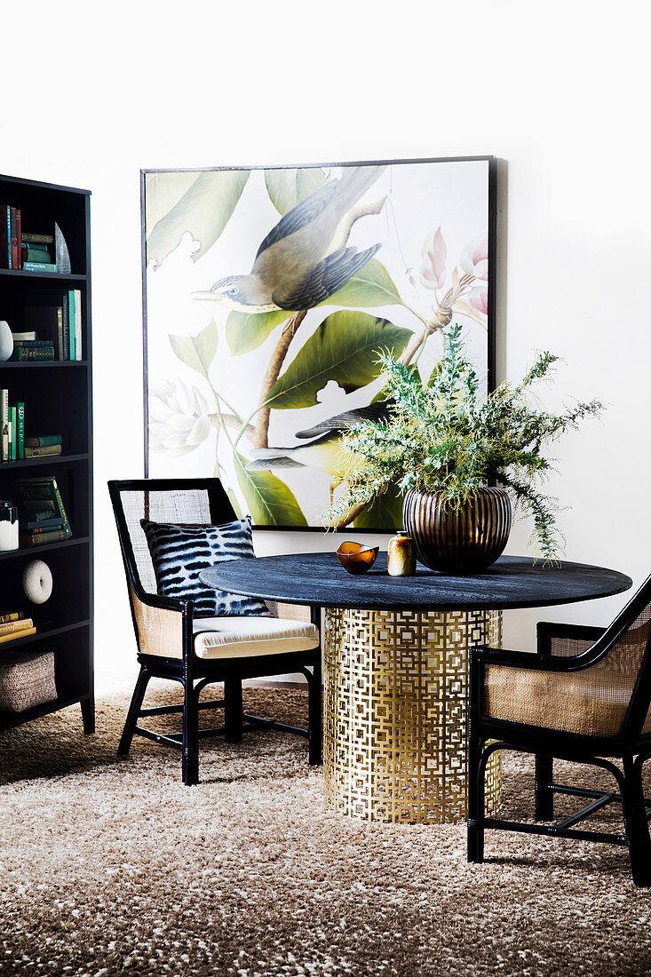 Upholstered chairs around a round dining table with a filigree metal base in front of a bird picture