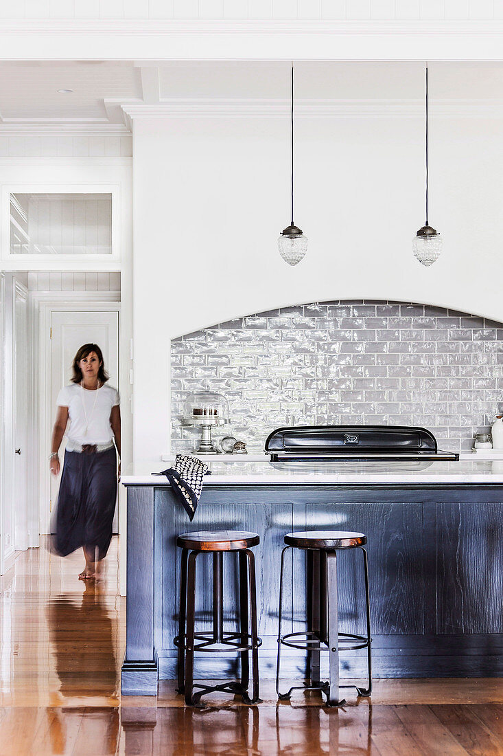 Counter with bar stools in open kitchen, woman in background