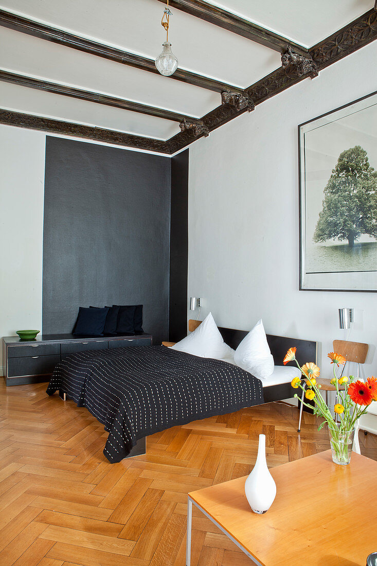 Doppelbett mit schwarzer Tagesdecke und Lowboard vor schwarzer Wand im Schlafzimmer