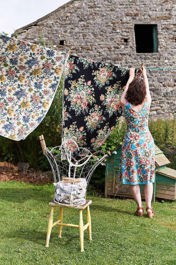 Frau im Blümchenkleid bei Wäscheaufhängen im Garten