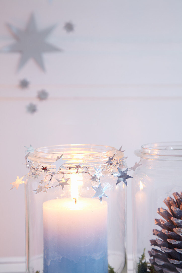 Festive arrangement of candle and pine cone in mason jars decorating with garland of stars