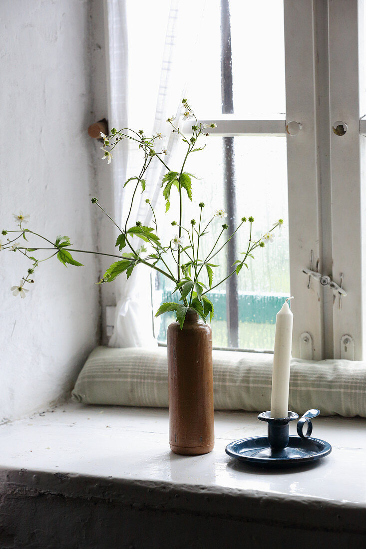 Kerzenhalter und Blütenzweige in Tonflasche auf Fensterbank