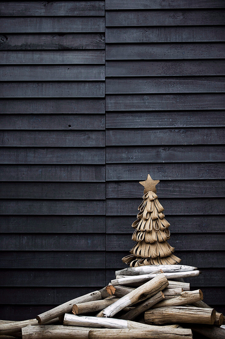 Stylized Christmas tree made of jute loops and driftwood sticks in front of a wooden wall on a terrace