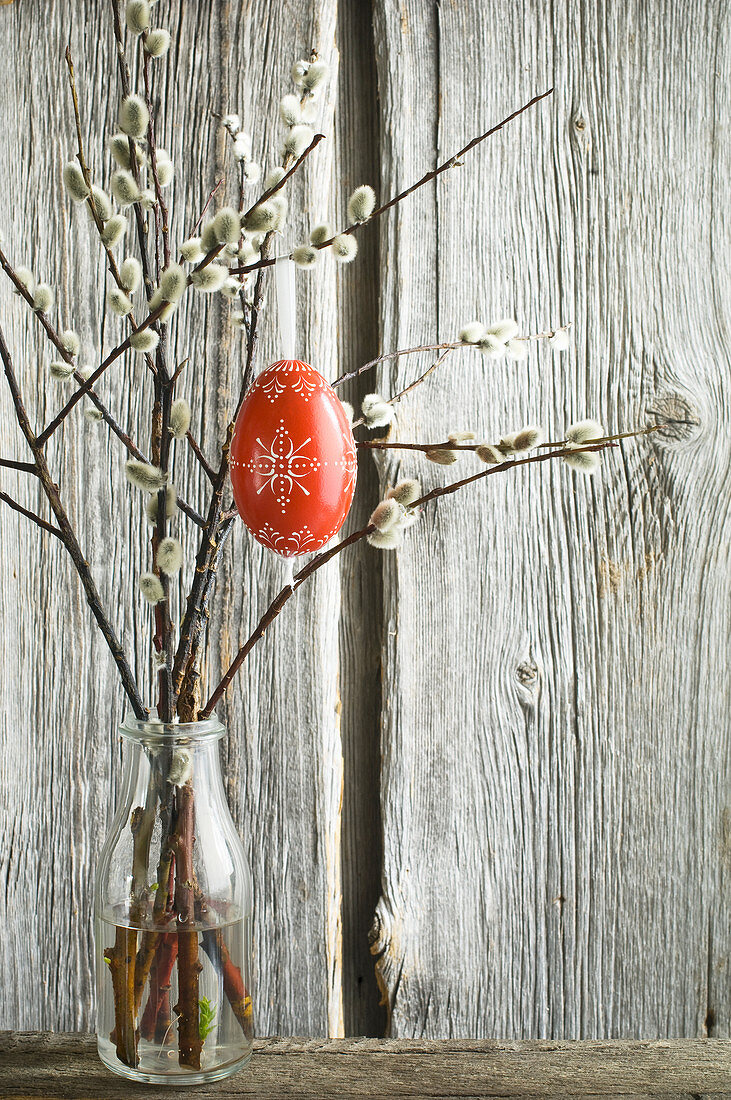 Red-painted Easter egg hung from pussy willow branches in bottle