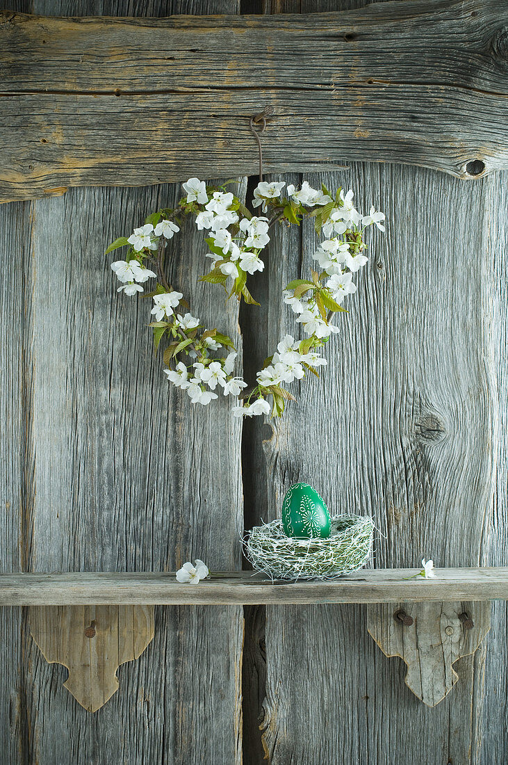 Kirschblütenkranz und handbemaltes grünes Osterei auf Regal vor rustikaler Holzwand