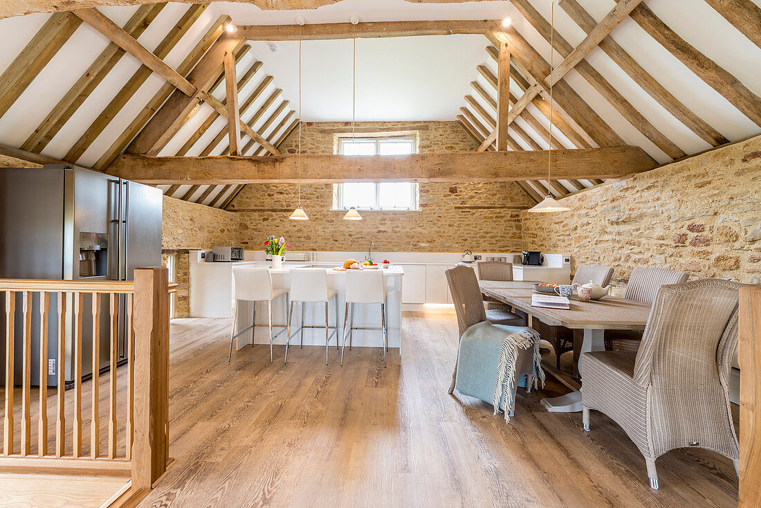 Open-plan kitchen and dining area below exposed roof structure in converted barn