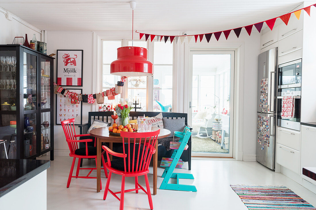 Weiße Wohnküche mit roter Weihnachtsdekoration, Esstisch mit Stühlen und Vitrinenschrank