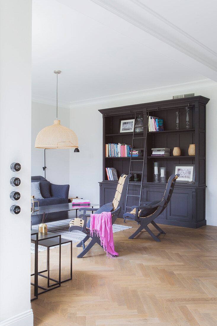 Chairs and coffee table in front of dark bookcase with library ladder in living room with herringbone parquet floor