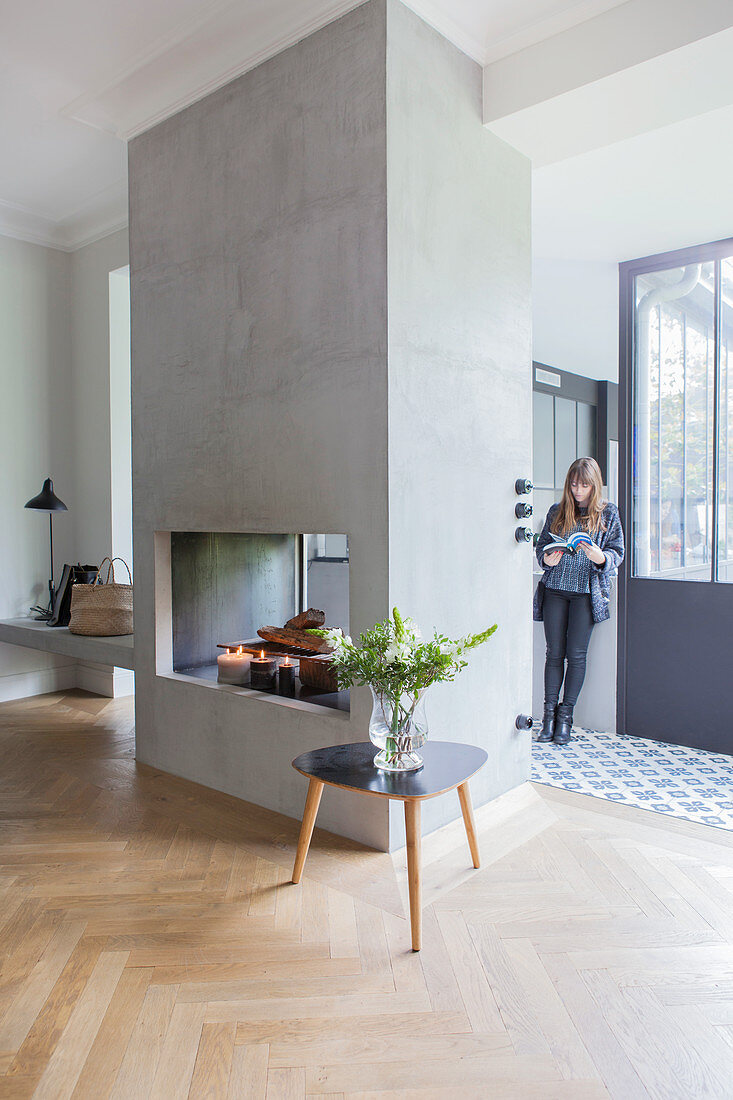 Coffee table in front of fireplace with woman in doorway in background