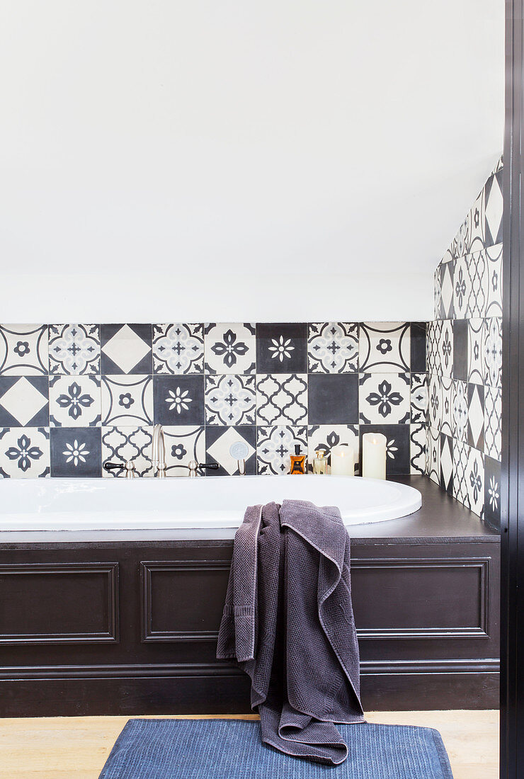 Bathtub with dark wood panelling in bathroom with black-and-white wall tiles