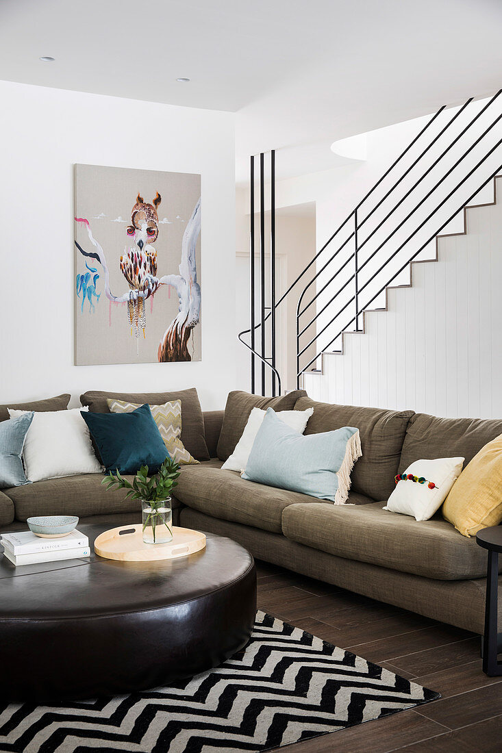 Gemütliche Sofagarnitur mit Kissen und Leder-Couchtisch vor Treppe im Wohnzimmer