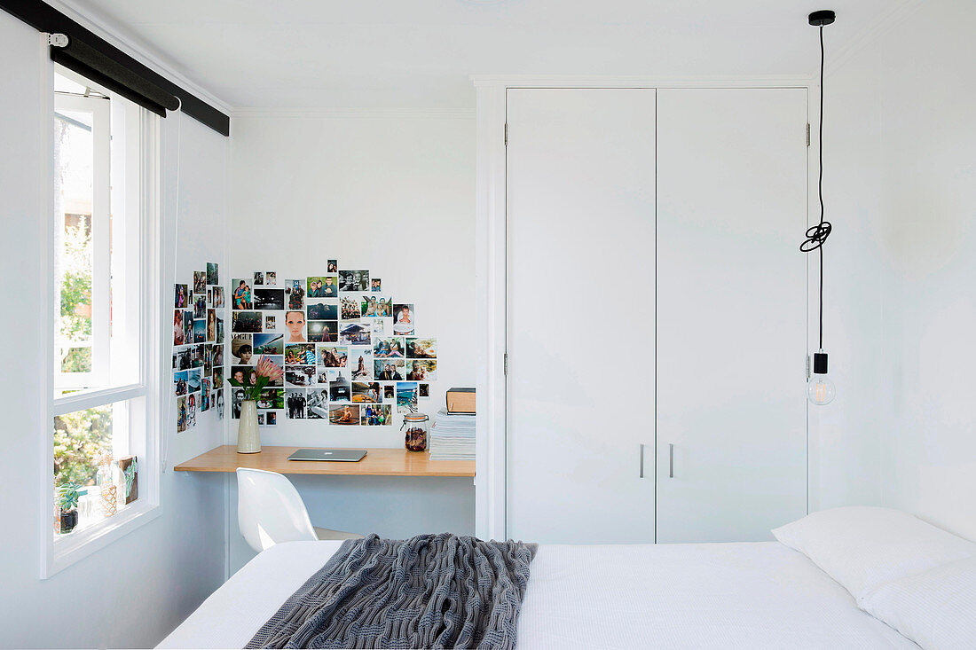 Doppelbett, Pendelleuchte, Einbauschrank, kleiner Schreibtisch und Fotogalerie an der Wand in weißem Schlafzimmer