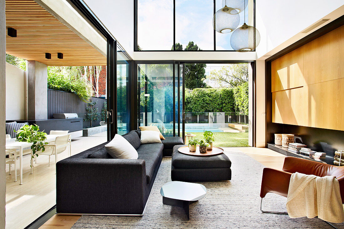 Elegantes Wohnzimmer mit doppelter Raumhöhe, offene Glasschiebetüren zum Garten und zur überdachter Terrasse