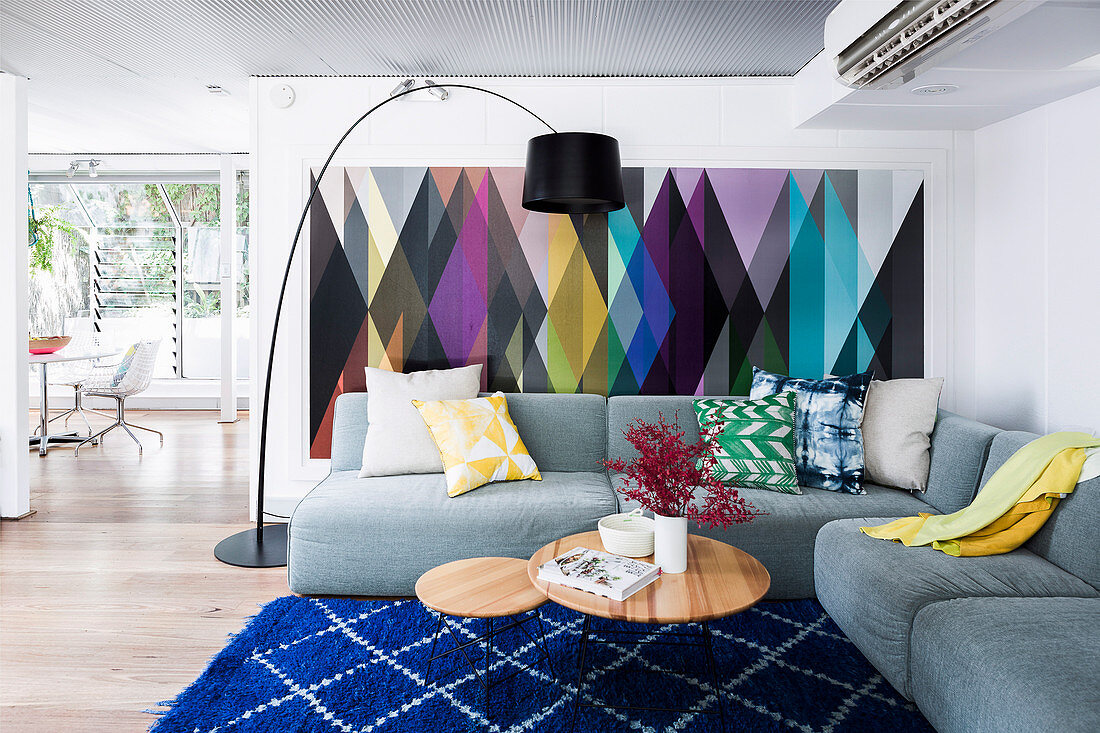 Gray upholstered sofa with cushions, coffee table and arc lamp in the living room, colorful wallpaper with a geometric pattern on the wall