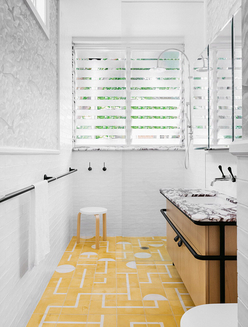 Vanity in front of shower and louvre window in bathroom with yellow and white tiled floor