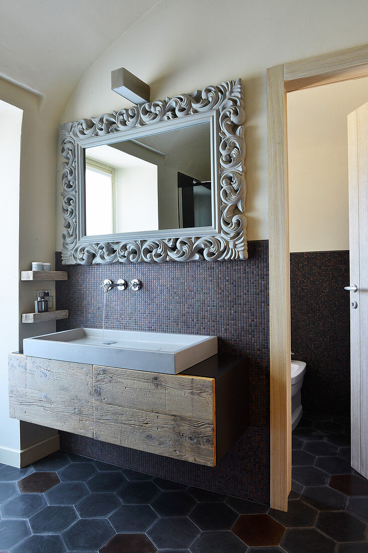 Mirror with artistic frame above concrete sink in designer bathroom with cement tiles