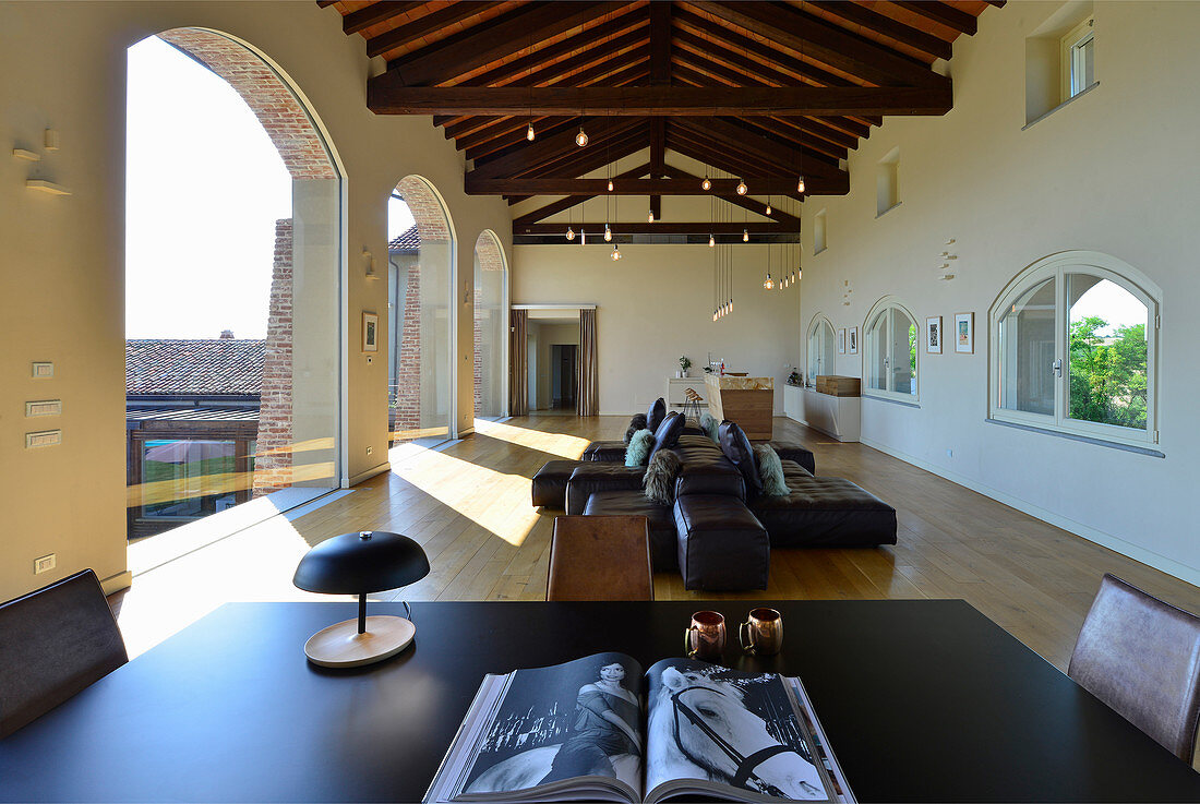 View across table to leather sofa set in elegant loggia with arches in renovated farmhouse