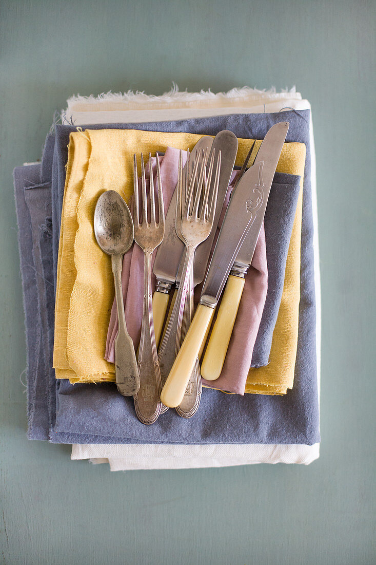 Old cutlery on stack of pastel cloths