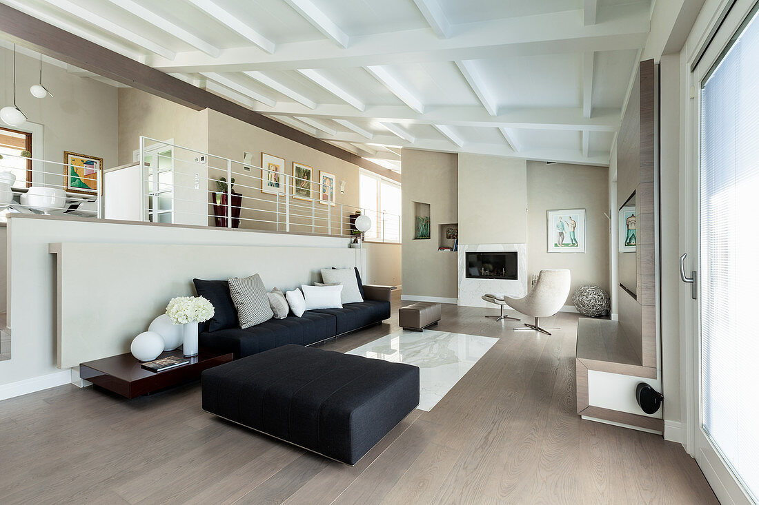 Modern, open-plan living room in black and white with corridor on gallery