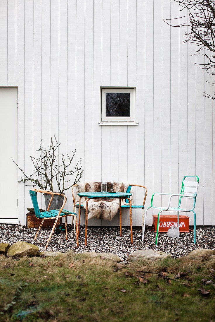 Vintage Gartenmöbel mit Fell vor weißem Holzhaus