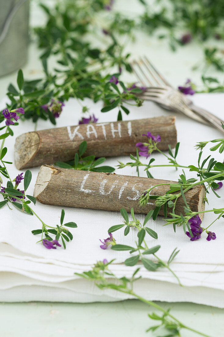 Place markers made from pieces of hazel wood decorated with purple-flowering alfalfa (Medicago sativa)