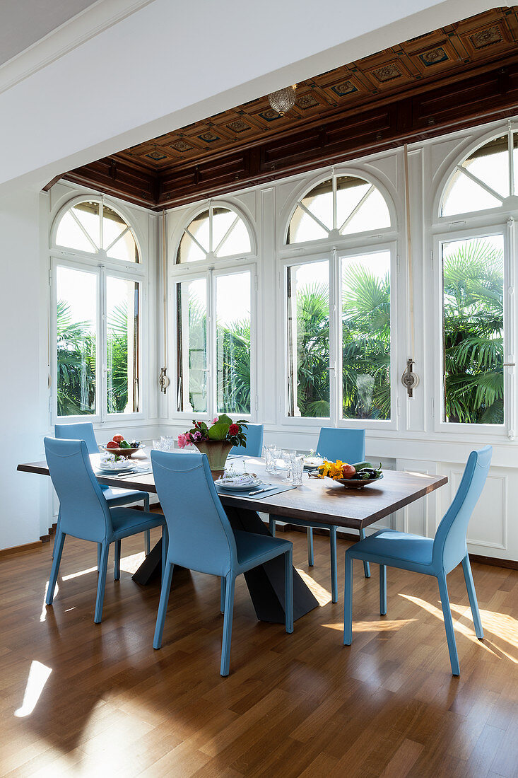 Blue chairs around dining table in window bay with arched windows